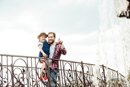 happy father holding little daughter in hands and pointing away in parkの写真素材