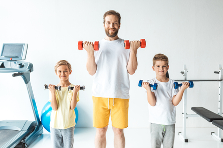 cheerful father and sons exercising with dumbbells and smiling at cameraの写真素材