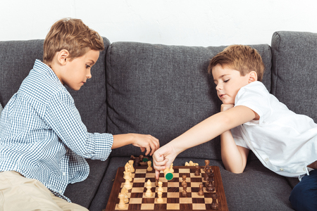 cute little boys playing chess while sitting on sofa at homeの写真素材