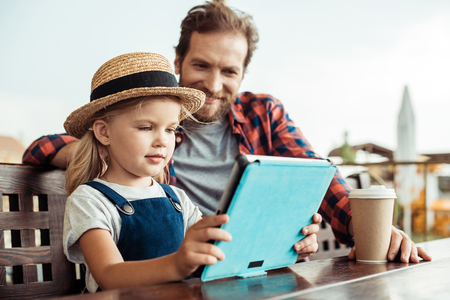 selective focus of little girl using tablet while father sitting near byの写真素材