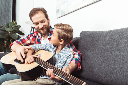 happy father and son playing guitar together at homeの写真素材
