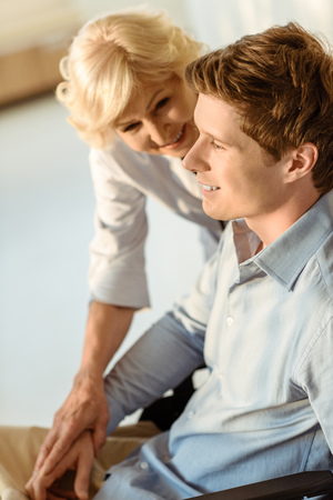 Smiling young man sitting down with elderly doctor holding his hand and smiling at himの写真素材