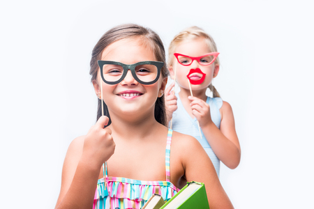 adorable little girls with party sticks and books smiling at camera isolated on whiteの写真素材
