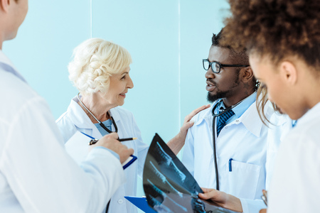 Senior doctor talking to african-american medical intern and touching him on shoulderの写真素材