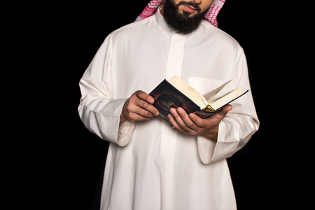 cropped shot of muslim man reading quran isolated on black の写真素材