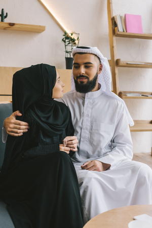 loving muslim couple sitting on sofa and embracingの写真素材