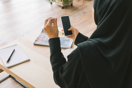 back view of young muslim woman using smartphone in cafeの写真素材