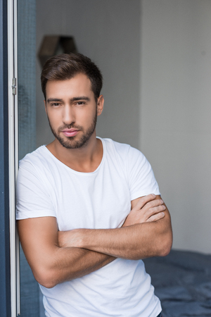 Young attractive man posing with arms crossed by the windowの写真素材
