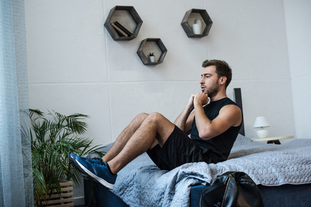 Young fit man in sportswear doing exercises on his bedの写真素材