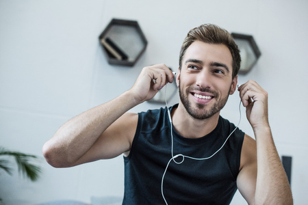 Young smiling man in tanktop putting on earbuds and looking asideの写真素材