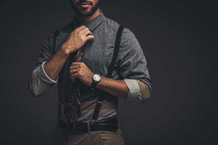 Cropped shot of young bearded man in suspenders adjusting his tieの写真素材