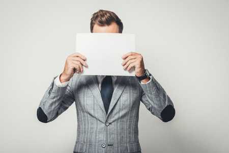 businessman in stylish suit covering face with blank paperの写真素材