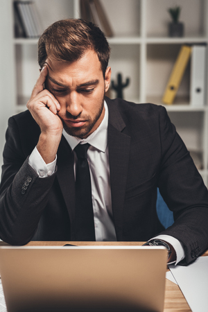 exhausted young businessman with headache working with laptopの写真素材
