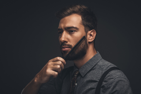 Young handsome man grooming his beard with a combの写真素材