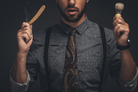 Cropped shot of young bearded man holding a straight razor and a shaving brushの写真素材
