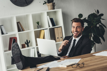 happy young businessman working with laptop on knees in modern officeの写真素材