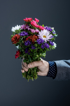 Cropped shot of man in suit holding a beautiful bouquet of colorful flowersの写真素材