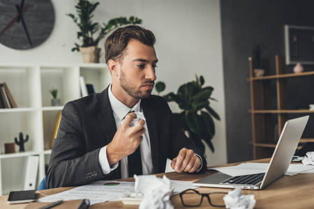 young businessman with crumpled papers on worktableの写真素材