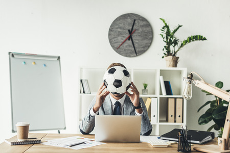 businessman covering face with soccer ball at modern officeの写真素材
