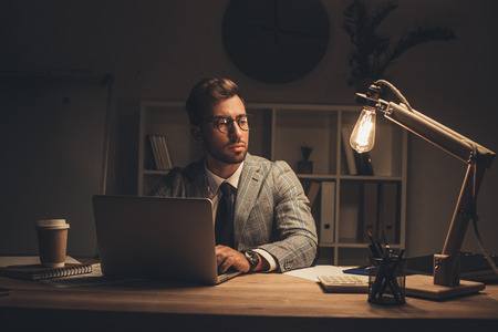 thoughtful young businessman working with laptop and looking awayの写真素材