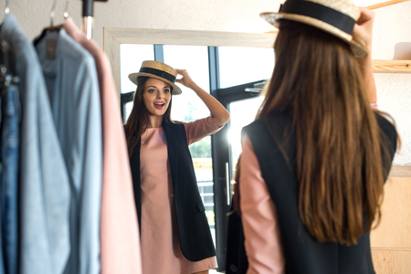 back view of smiling young woman trying on hat in boutiqueの写真素材