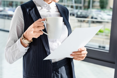 Cropped shot of young businesswoman at her office holding some paperwork and cup of coffeeの写真素材