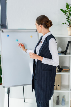 Young businesswoman in office doing a presentation and writing with marker on whiteboardの写真素材