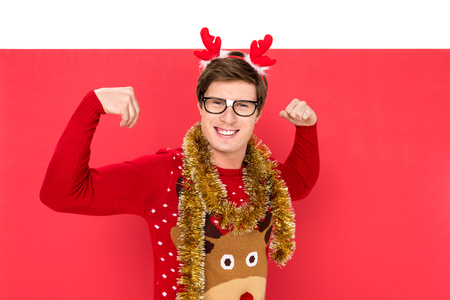 portrait of man in winter sweater with decorative deer horns on head showing musclesの写真素材