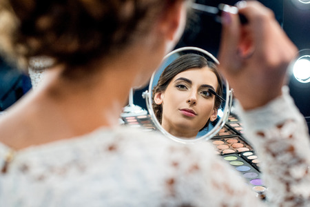 mirror reflection of young woman looking in mirror and applying mascara in beauty studioの写真素材