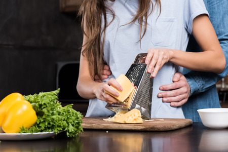 cropped shot of boyfriend hugging girlfriend while she grating cheese for dinnerの写真素材
