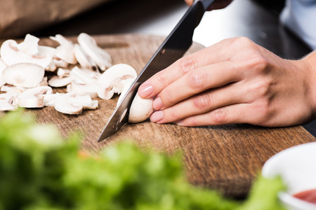 partial view of woman cutting mushrooms while cooking dinnerの写真素材