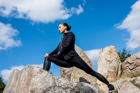 bottom view of young fit woman stretching legs on rocks
