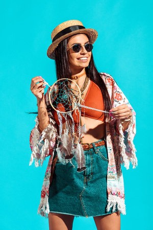 Stylish bohemian girl holding dreamcatcher isolated on turquoiseの写真素材