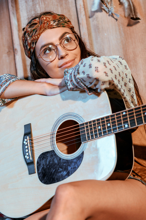 Attractive hippie girl in headband and glasses sitting with a guitar in wooden house の写真素材