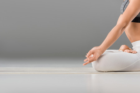 cropped shot of young woman performing lotus pose on greyの写真素材