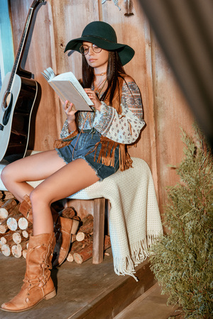 Attractive bohemian girl reading a book sitting on a bench in a wooden houseの写真素材