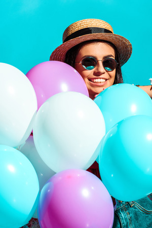 Smiling bohemian girl standing with helium balloons isolated on turquoise の写真素材