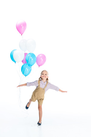 adorable little girl holding colorful balloons and smiling at camera isolated on whiteの写真素材