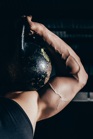 Cropped shot of athletic sportsman with embossed muscles holding a kettlebell on his shoulderの写真素材