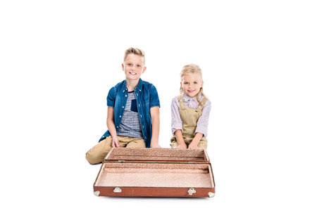 adorable little children sitting near empty suitcase and smiling at camera isolated on whiteの写真素材