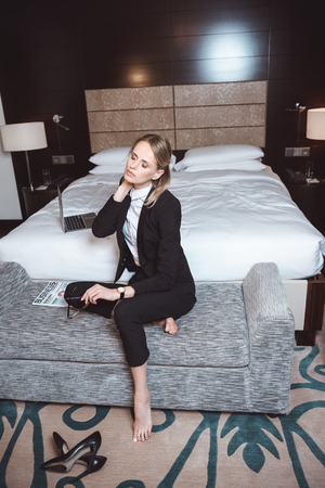 overworked barefoot young businesswoman sitting on couch in hotel roomの写真素材