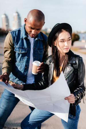 portrait of multicultural couple with map in hands standing on streetの写真素材