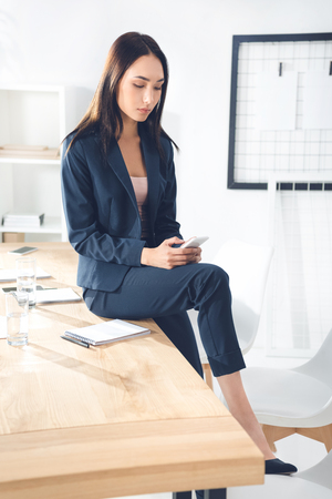 businesswoman using smartphone while sitting on table at officeの写真素材