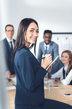 businesswoman writing in notebook in conference hall with blurred colleagues on backgroundの写真素材