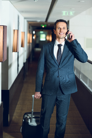 businessman walking down hotel corridor with a suitcase and talking on phoneの写真素材