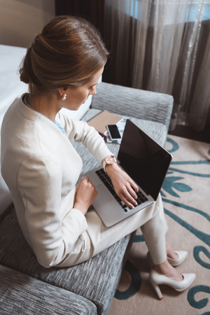 young businesswoman using laptop and checking wristwatch in hotel roomの写真素材