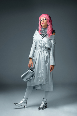 fashionable girl in pink wig and eyeglasses posing with watering can isolated on greyの写真素材