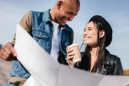 portrait of multicultural couple with map in hands standing on street