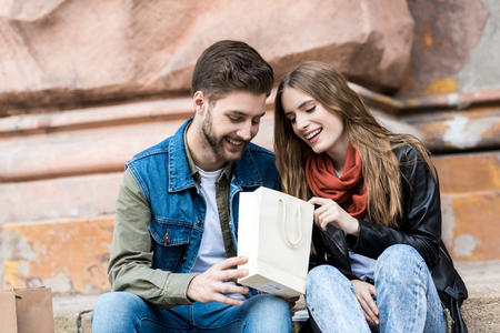 portrait of smiling couple looking into shopping bag together on streetの写真素材