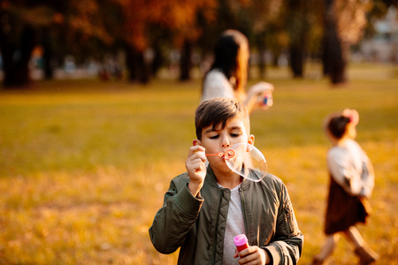 Little boy in an autumn jacket playing with soap bubbles in parkの写真素材